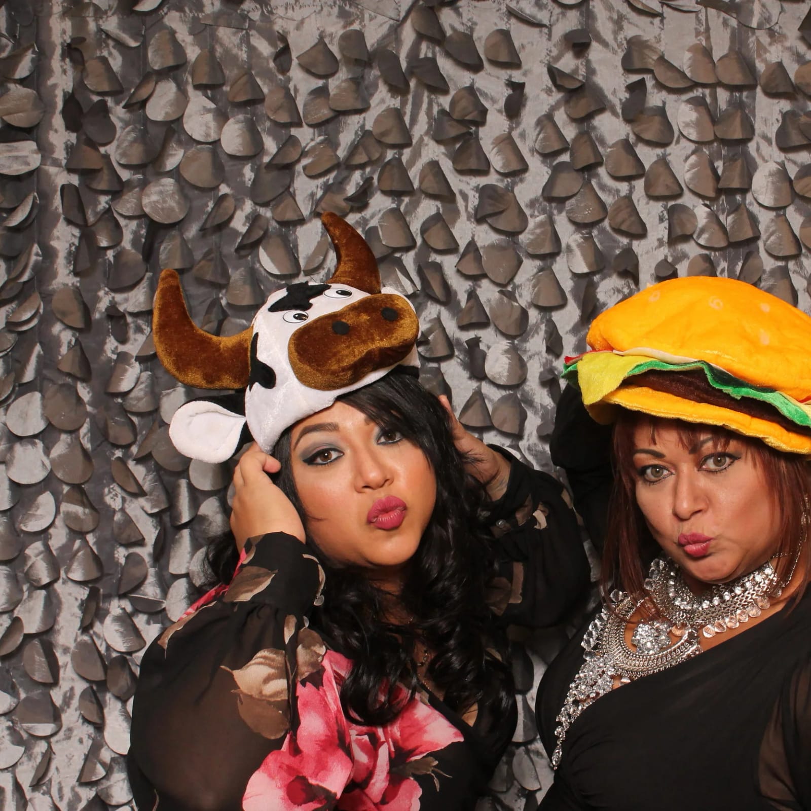 Two guests in animal and food hats posing against a sequin backdrop