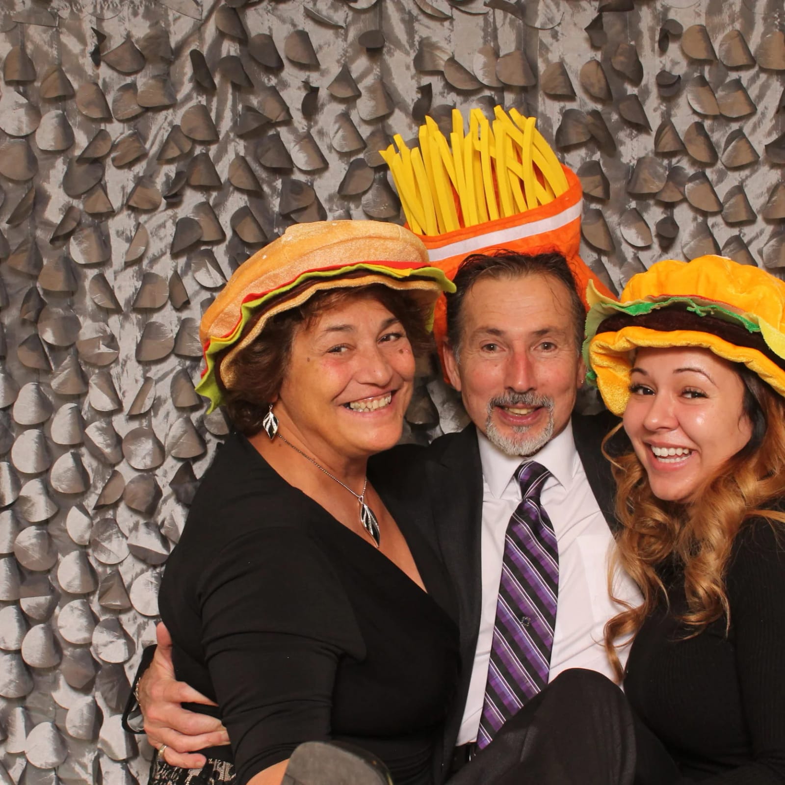 Three guests in burger and fries hats smiling in the booth